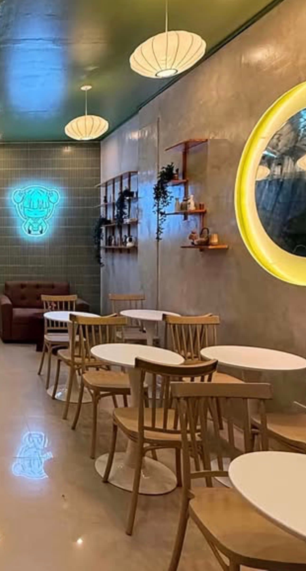 Interior of a Natsu Café — warm wood chairs, round tables, paper lanterns and a glowing mascot sign