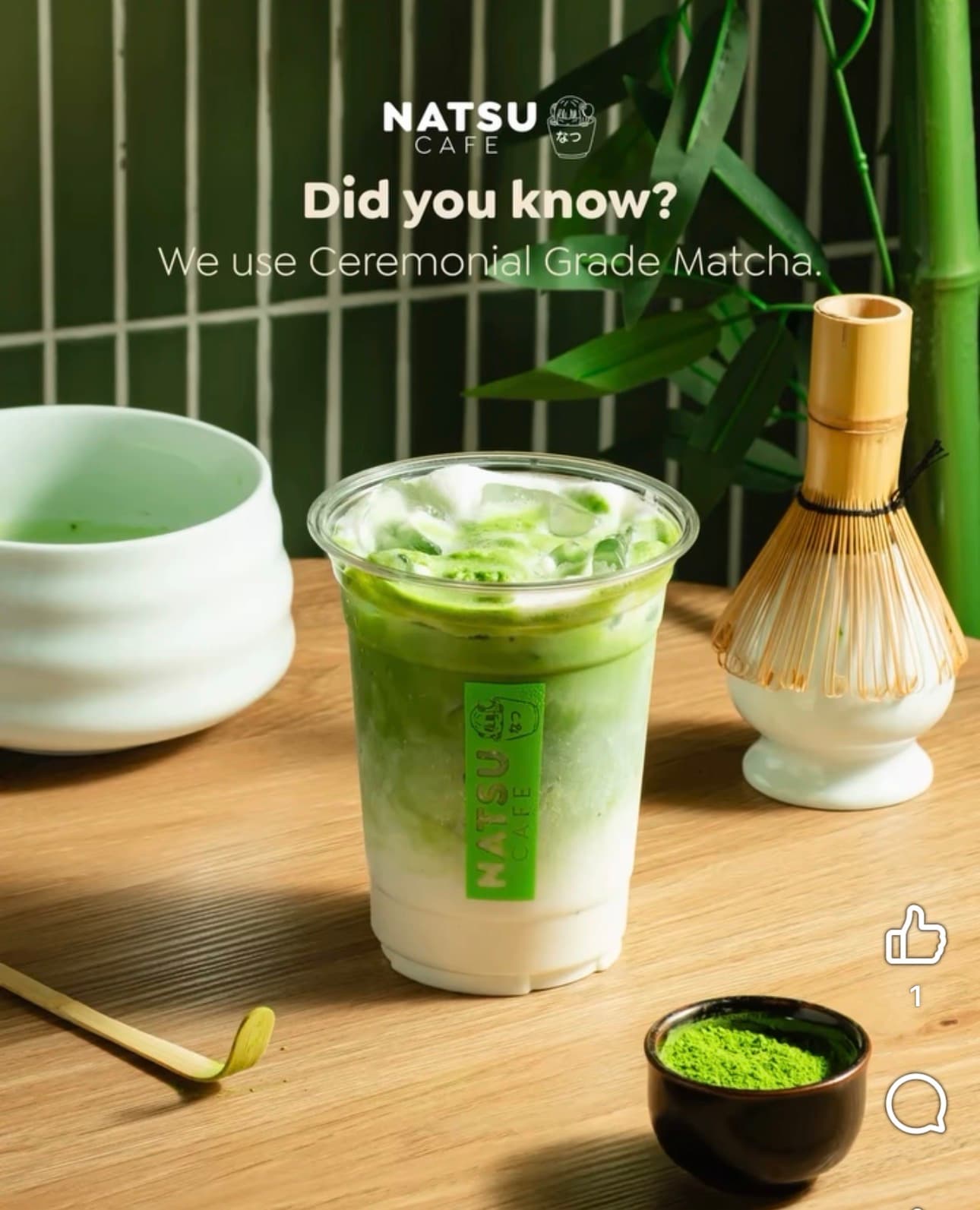 An iced Natsu Café matcha latte beside a bamboo whisk, scoop, and bowl of matcha powder